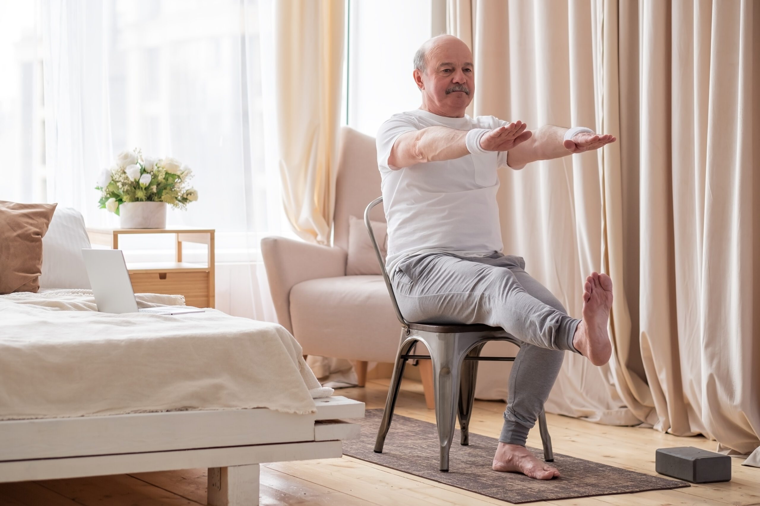 Elderly man practicing yoga for legs and hands using chair.