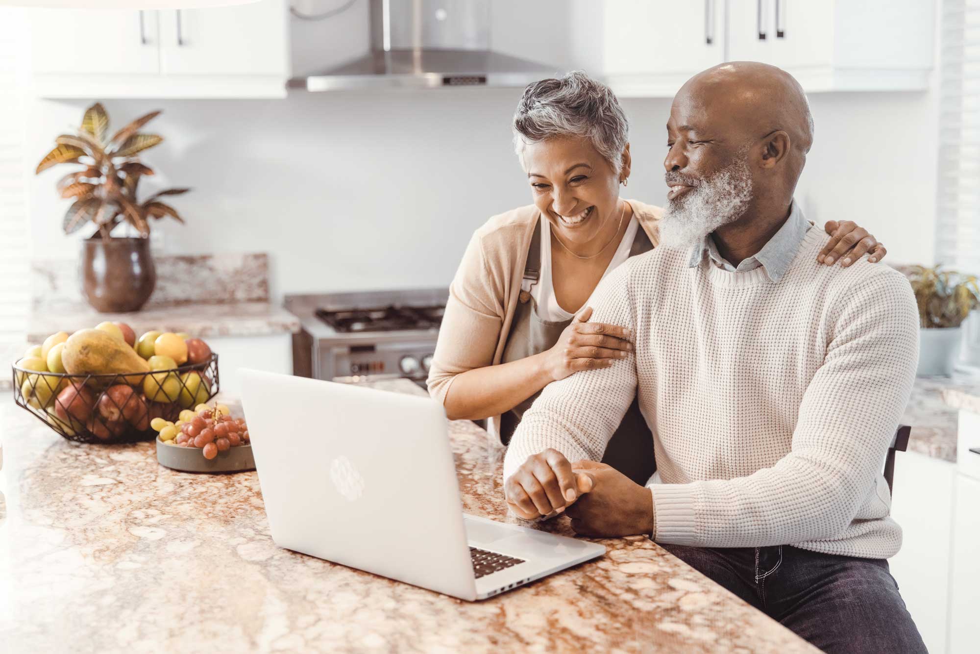 a senior couple browsing on their laptop while seated at the kitchen island